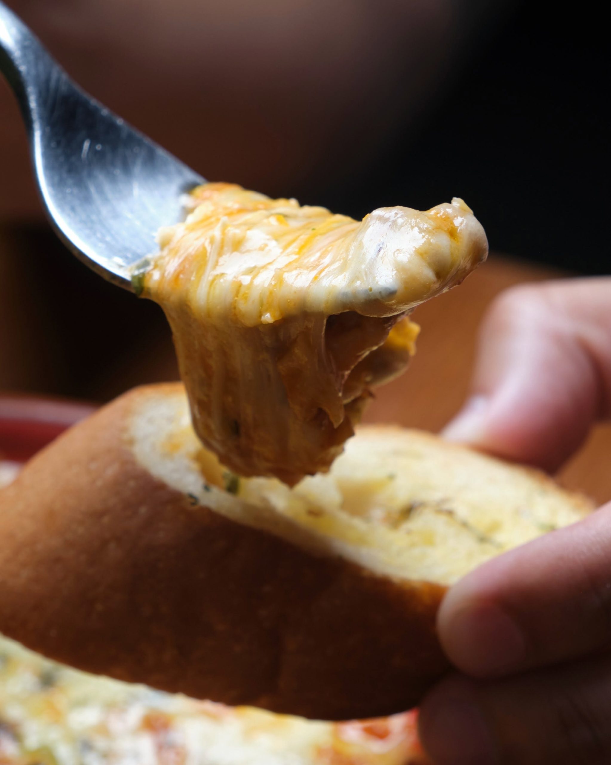 Tenedor con un bocado de lasaña mixta de pollo y carne con mozzarella fundida sobre una rebanada de pan de ajo