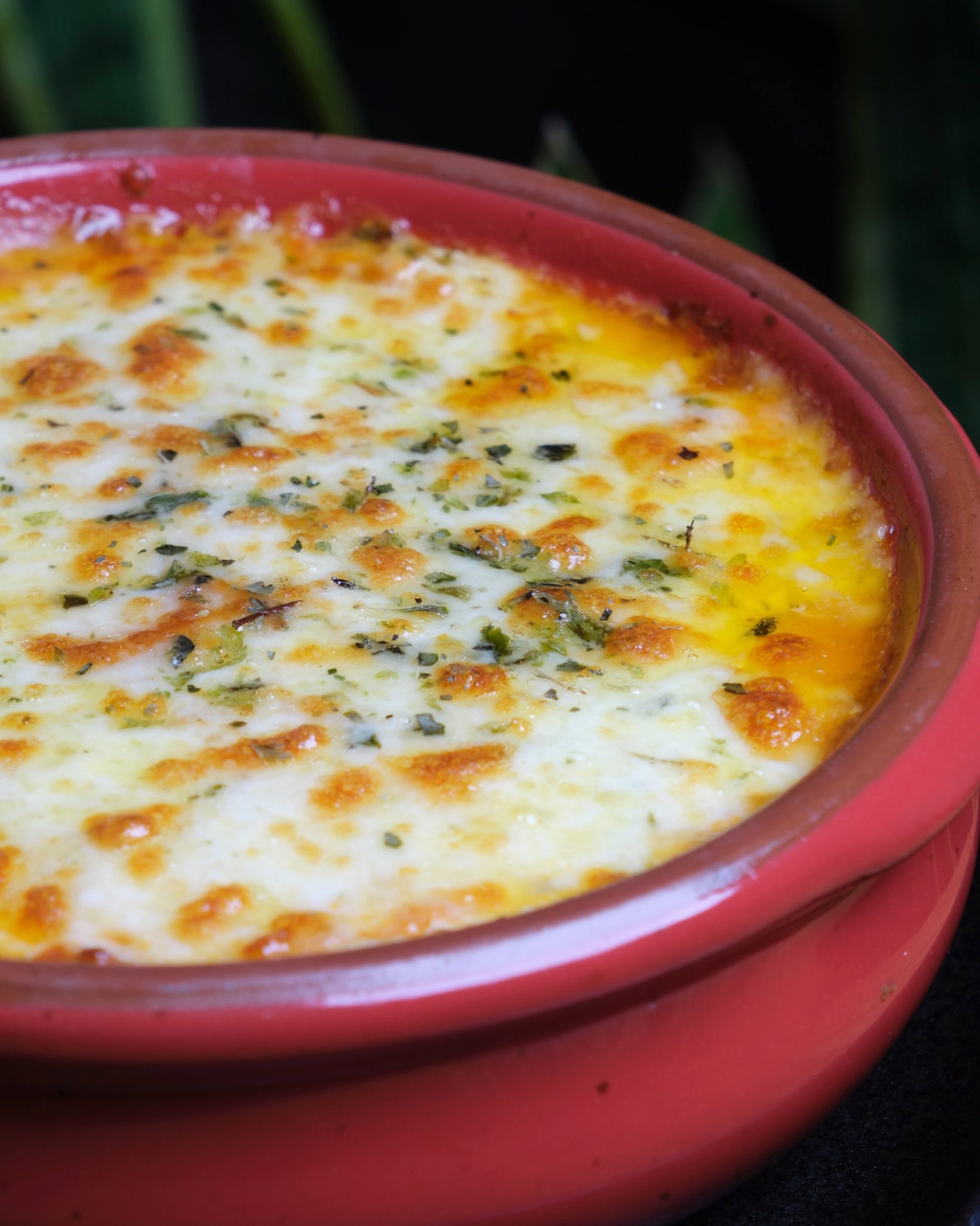 Detalle del gratinado dorado de mozzarella con orégano sobre la lasaña mixta de pollo y carne